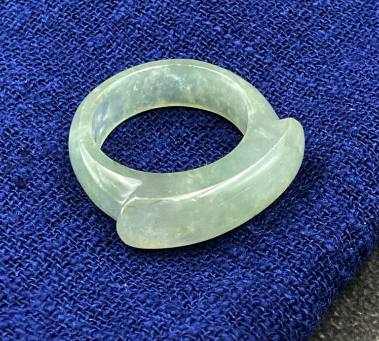 A stunning icy white jadeite saddle ring, showcasing its translucent, smooth texture and elegant saddle-shaped design, resting on a soft fabric background.
