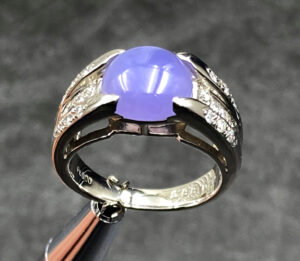 A stunning close-up of the Natural Ice-type Violet Jade Cabochon Ring, showcasing its translucent violet hue, 22K white gold band, and sparkling diamond accents on a velvet background.