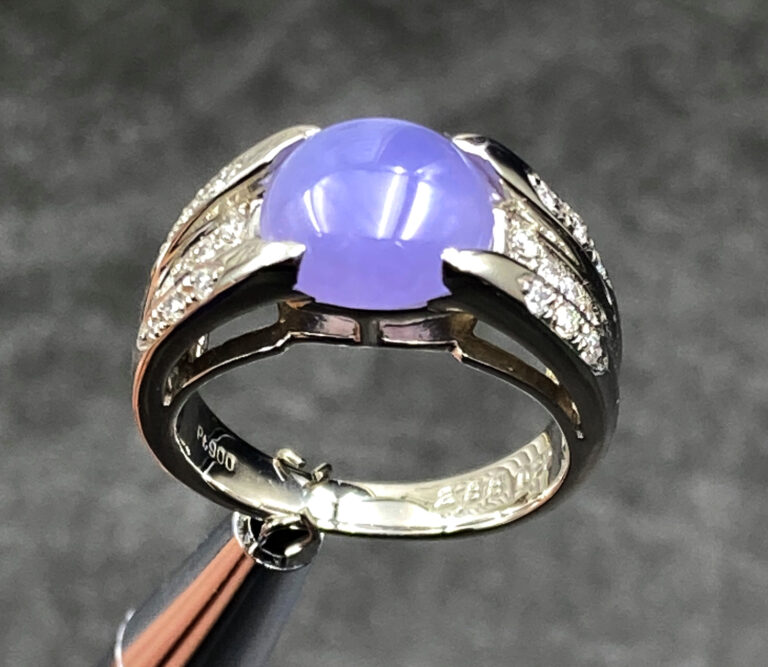A stunning close-up of the Natural Ice-type Violet Jade Cabochon Ring, showcasing its translucent violet hue, 22K white gold band, and sparkling diamond accents on a velvet background.