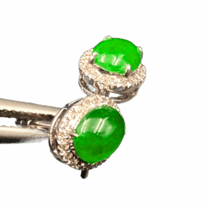 A pair of elegant oval-shaped icy jadeite earrings with a vibrant green hue, set in 18K white gold and surrounded by brilliant diamonds, showcasing a luxurious and harmonious design.
