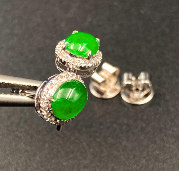 A pair of elegant oval-shaped icy jadeite earrings with a vibrant green hue, set in 18K white gold and surrounded by brilliant diamonds, showcasing a luxurious and harmonious design.