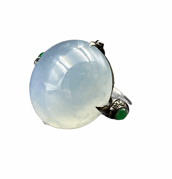 A stunning close-up of the Natural Ice White Jadeite Cabochon Ring, showcasing its smooth, translucent jadeite centerpiece set in sleek black 18K gold, accented with sparkling diamonds and vibrant green jadeite side stones.