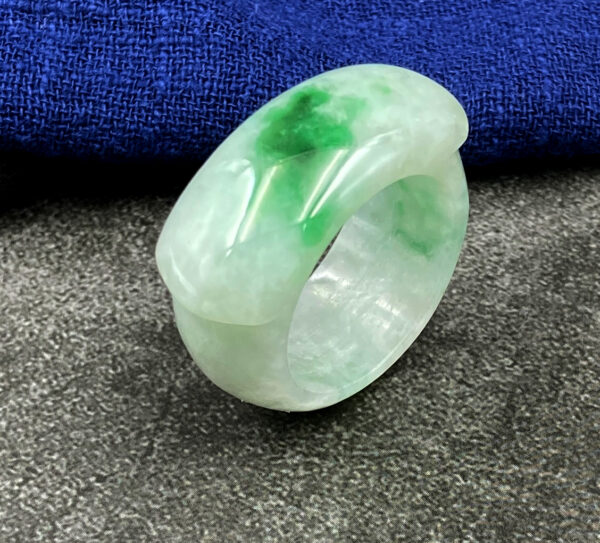 A smooth, polished natural jadeite saddle ring with delicate green hues, resting on a soft fabric background, showcasing its classic and minimalist design.