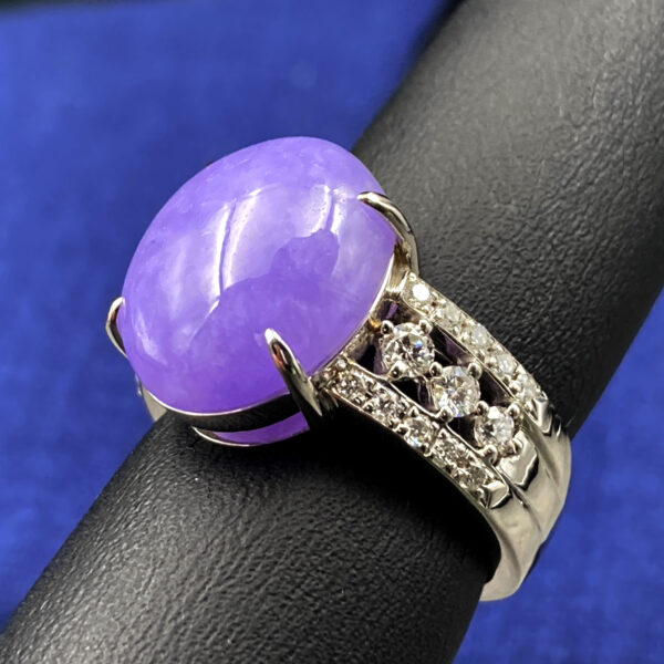 A stunning natural ice-type violet jadeite cabochon ring with a delicate pale purple hue, set in platinum and accented with sparkling diamonds on both sides of the band.