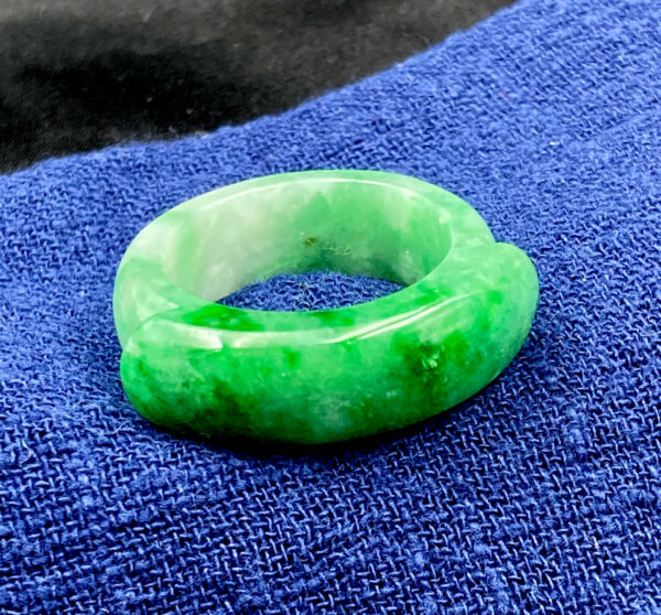 A stunning natural jadeite saddle ring featuring a rich, translucent green hue, meticulously polished for a glossy finish. The curved design rests comfortably on the finger, showcasing the pure beauty of jadeite without metal settings.