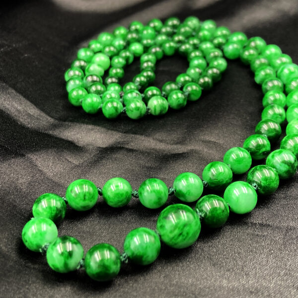 A stunning close-up of the Natural Jadeite Flower-Green Pagoda Beads Necklace, highlighting the rich emerald-green hues and intricate natural patterns of each jadeite bead. The necklace is elegantly draped, showcasing its smooth polish and lustrous glass-like finish.