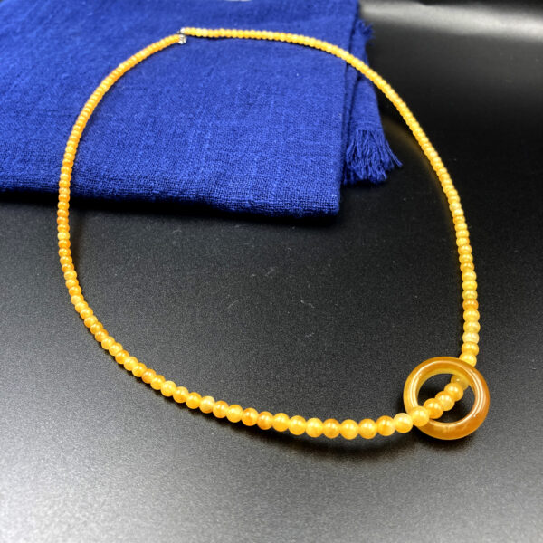 A stunning Natural Ice Yellow Jade Necklace featuring smooth, gradient-hued beads and a polished circular pendant, elegantly draped on a neutral background.