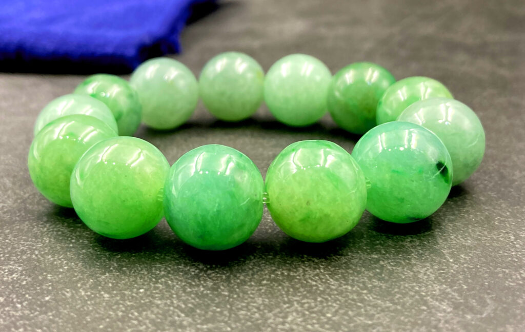 A stunning Ice-Type Jadeite Bracelet with 13 translucent beads (16mm each), showcasing floating green patterns against a cool, glassy background. The smooth, polished finish highlights its natural elegance.