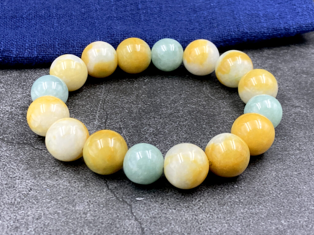 A stunning tri-color jadeite beaded bracelet showcasing harmonious yellow, white, and light green hues. Each 12mm bead is polished to a glossy finish, strung on an elastic cord for adjustable comfort. Perfect for gifting or personal collection.