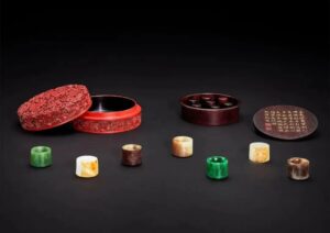 A complete set of seven Qianlong-period imperial jade thumb rings carved from Burmese jadeite and Hetian nephrite, presented in their original carved zitan box decorated with red lacquer and three fish amid falling blossoms; sold for HKD 64.936 million.