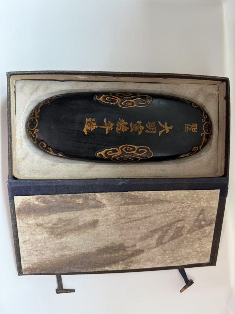 A finely carved Ming Dynasty Xuande Ink Cake featuring elegant cloud patterns and gold-traced characters "大明宣德年造," showcasing its deep black luster and historical craftsmanship.