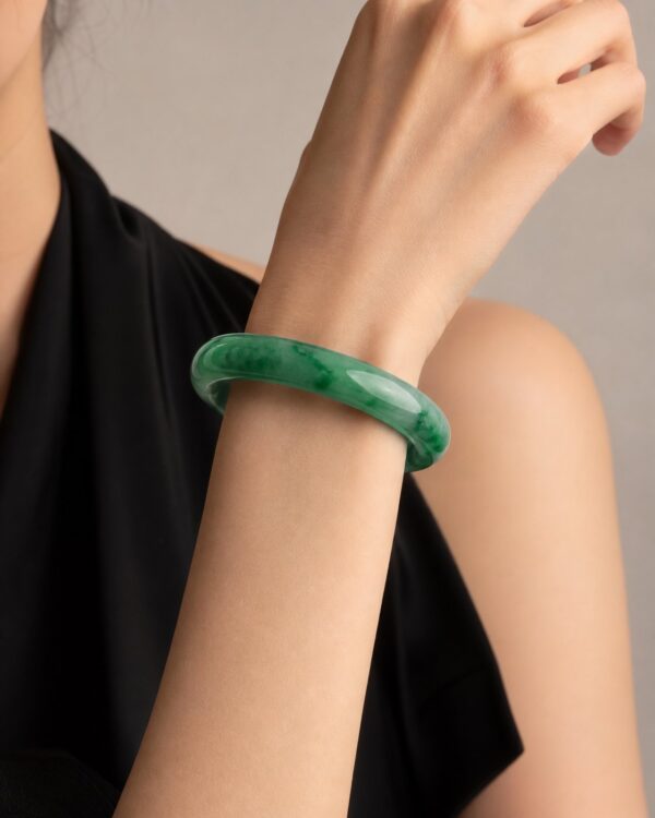 Close-up of polished green jade bangle on dark silk, soft light highlighting translucency