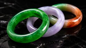 Luxurious jadeite bangles in green, violet, and tricolor arranged on silk