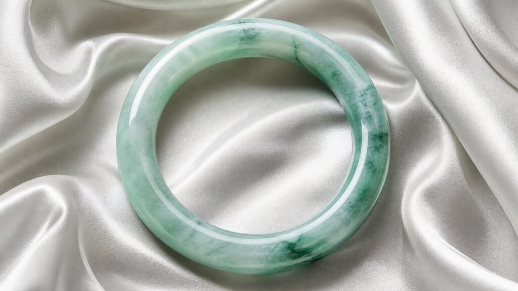 Close-up of a polished jadeite cabochon ring on a smooth grey surface, soft shadows emphasizing its rich green translucency