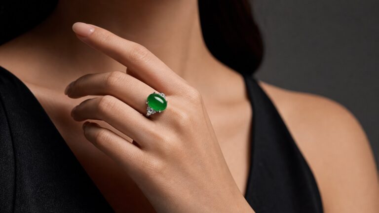 Luminous green jadeite cabochon ring on silk, soft light highlighting its translucency and smooth polish