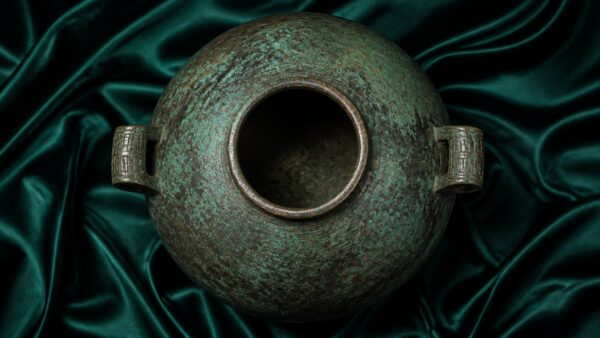 Ancient Chinese bronze vessel with verdigris patina, softly lit on dark silk
