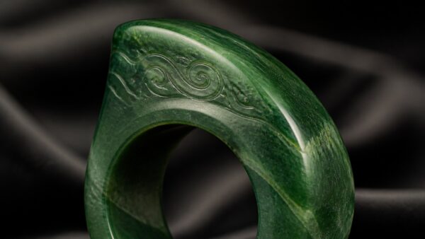A jadeite saddle ring on a silk display stand, softly lit to highlight its translucent green tones
