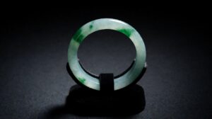 A translucent icy jadeite bangle with drifting green patches rests on dark silk under soft light
