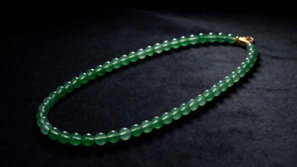 A single strand of polished green jadeite beads resting on soft cream silk in warm light