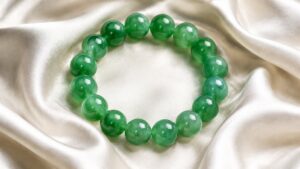 Polished jadeite bead bracelet draped over a pale wrist against soft neutral fabric, showing bead size and fit in elegant nat