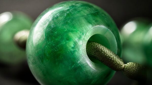 Polished jadeite beads arranged on a soft cloth beside a fine cord, lit to show their translucence and color in an elegant, c